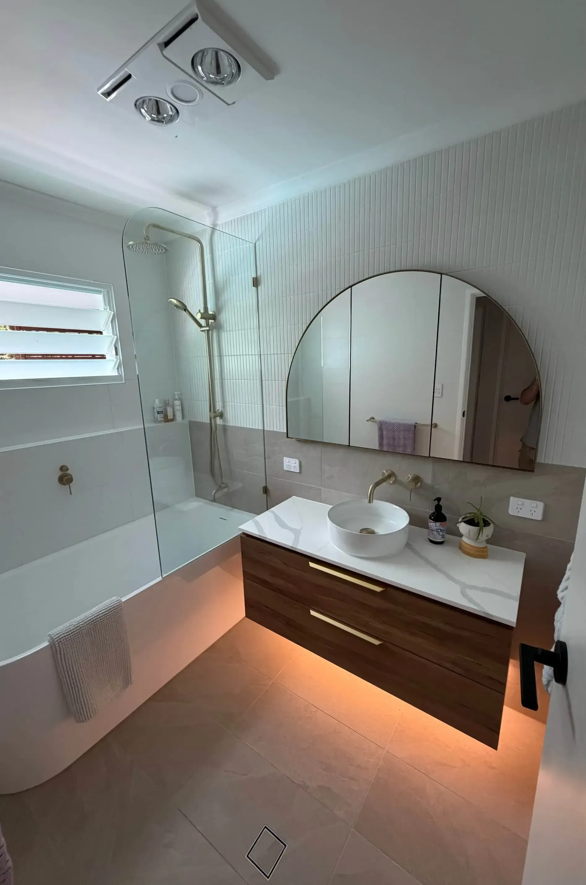 Modern bathroom with a bathtub, shower, vanity, and large arched mirror.