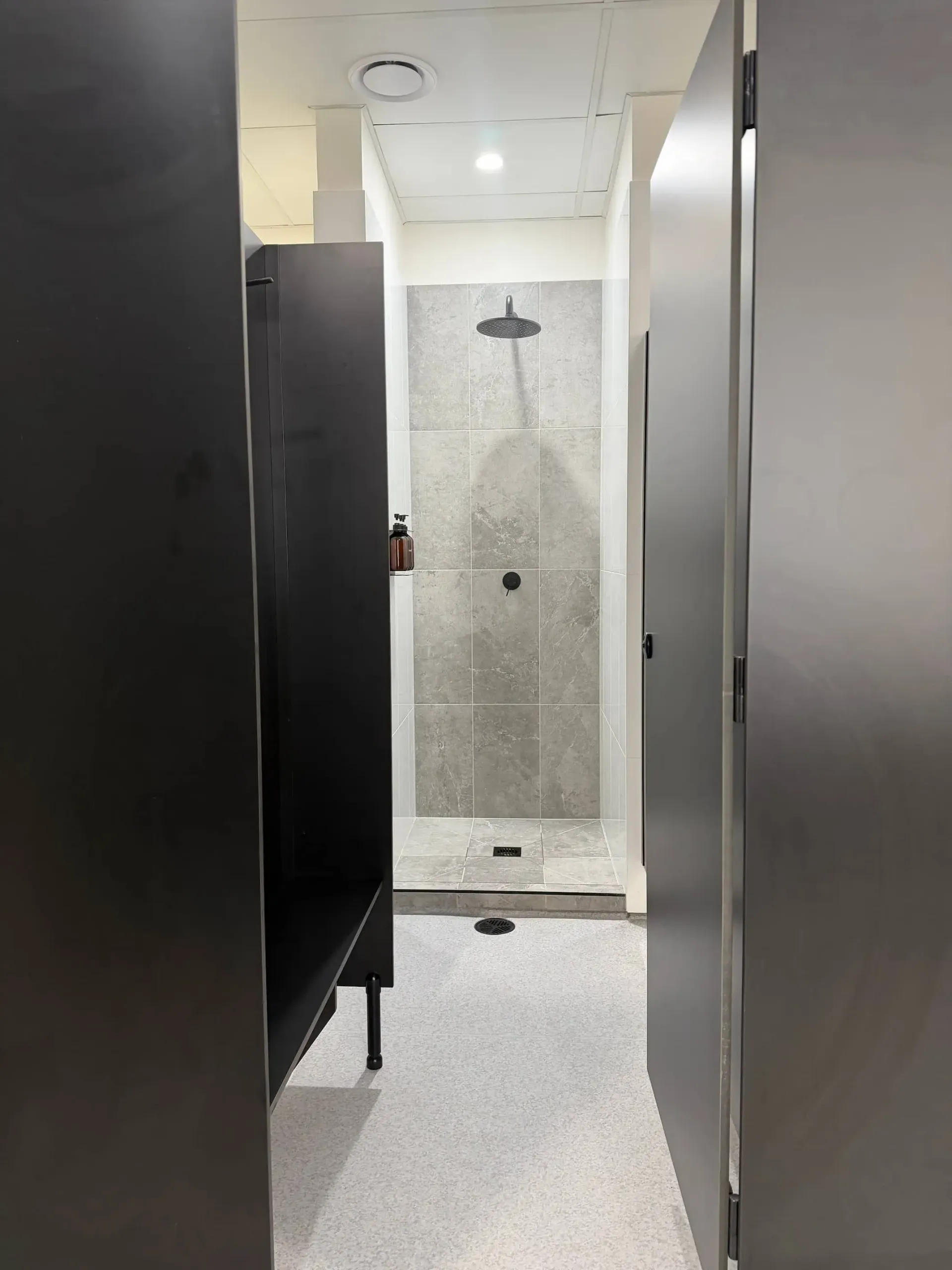 Shower stall hallway with black doors and gray tiled shower.