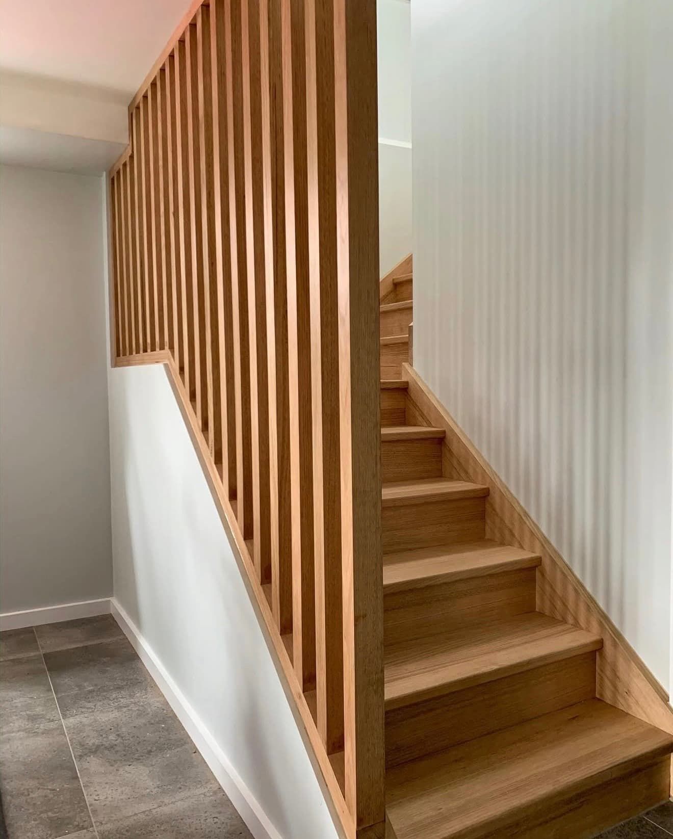 Wooden staircase with vertical slat railing and light gray walls.