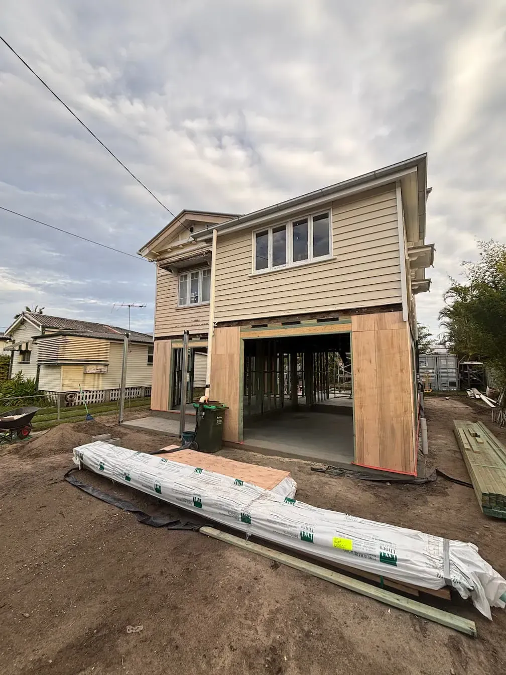 Two-story house under construction with exposed framing and beige siding.