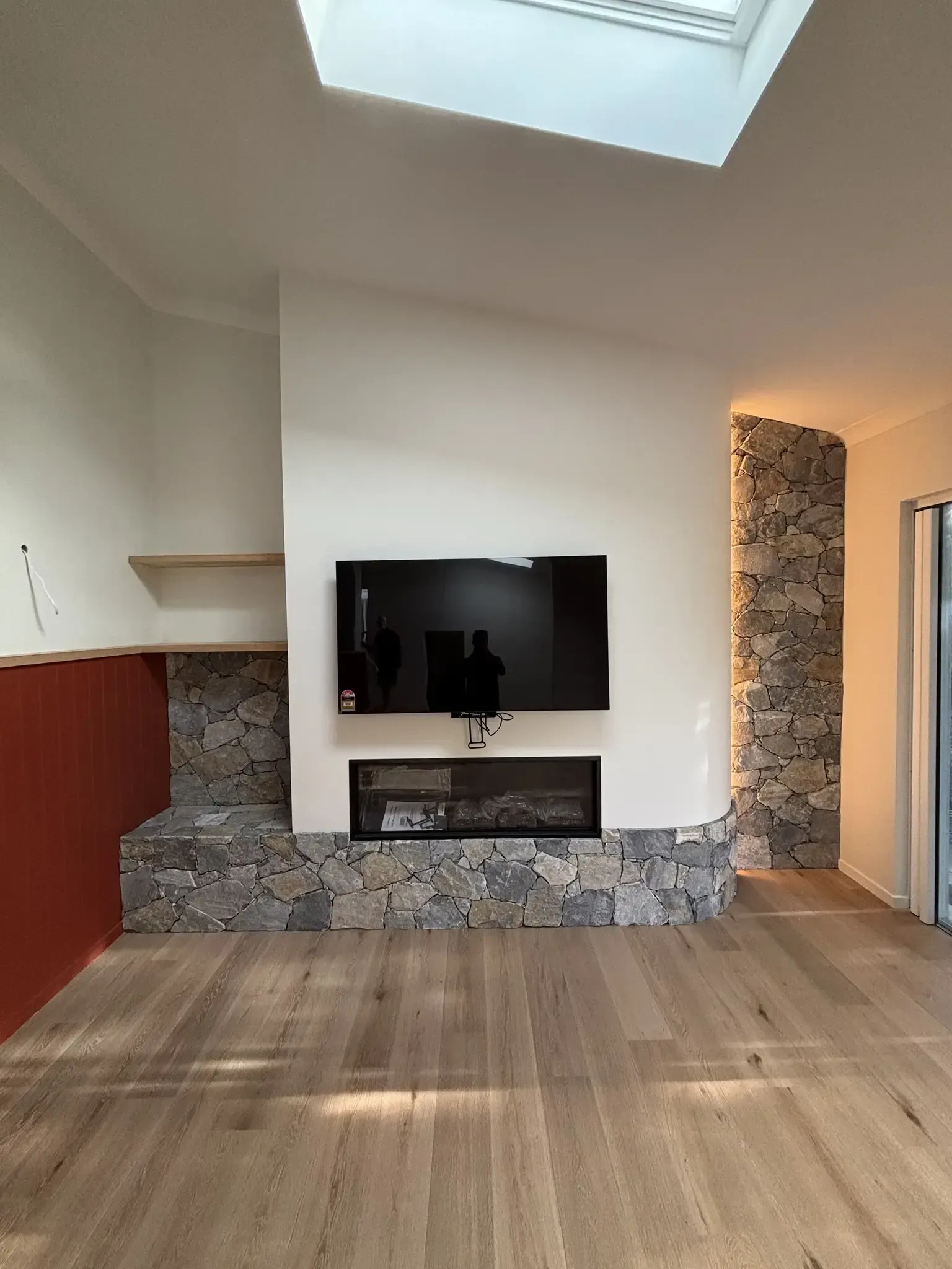 A living room with a fireplace and television. The fireplace has stone accents, a TV mounted above it, and hardwood floors.