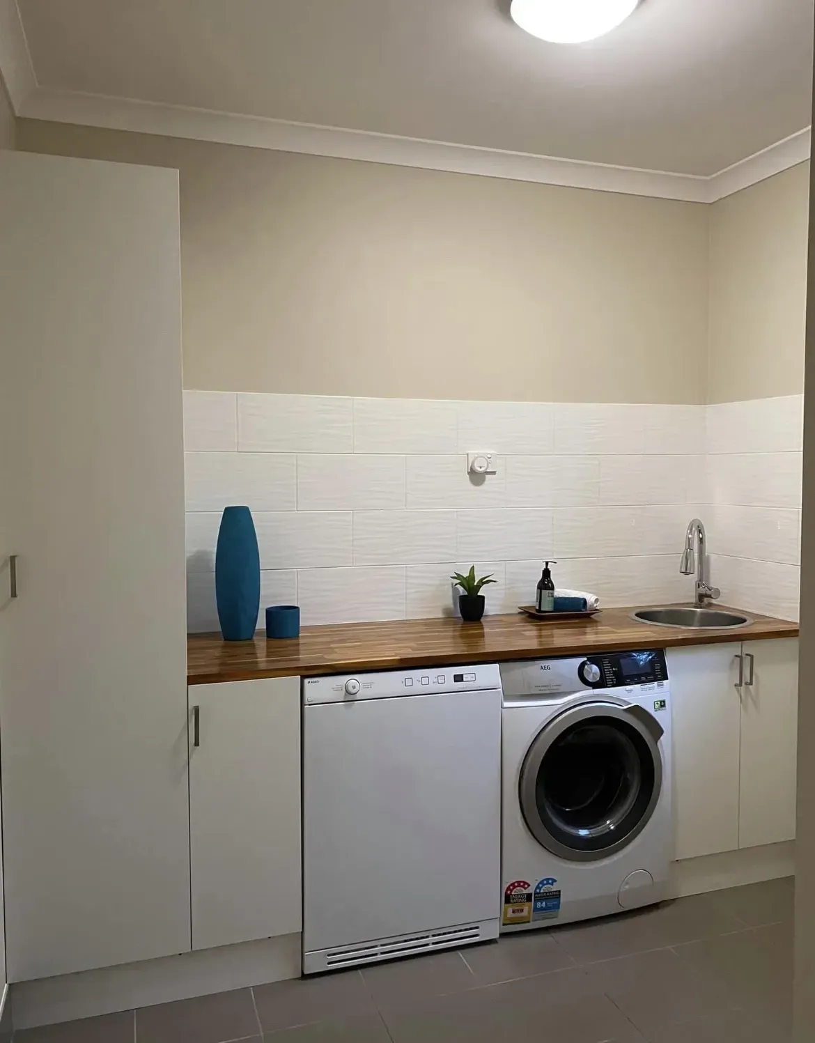 Laundry room with a washing machine, dryer, sink, cabinets, and decorative vase.