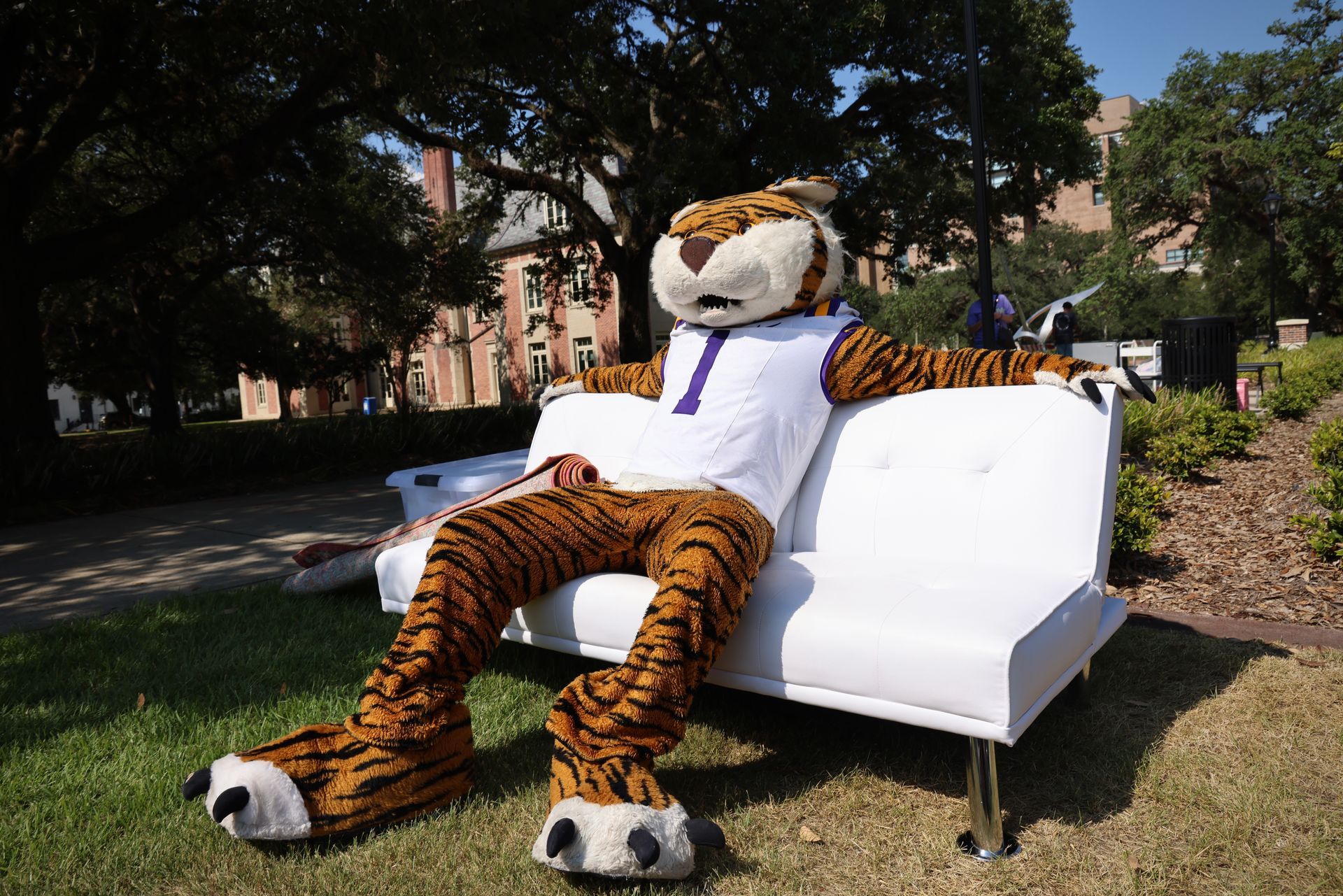 Tiger mascot lounging on a white couch outdoors in a sunny park