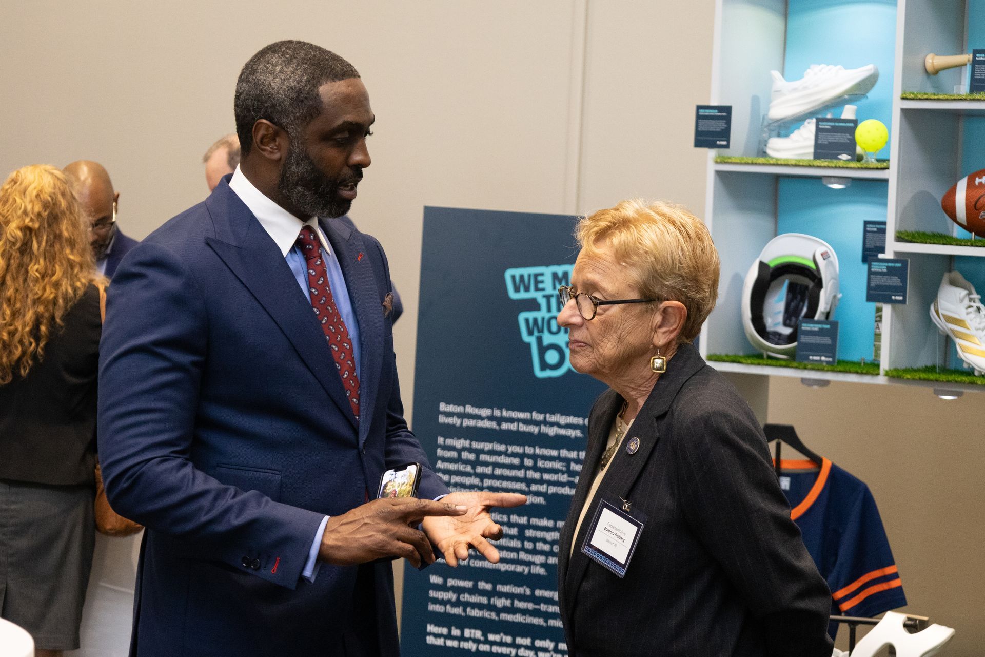 Two people talking at a booth, with promotional signage and display shelves in the background.