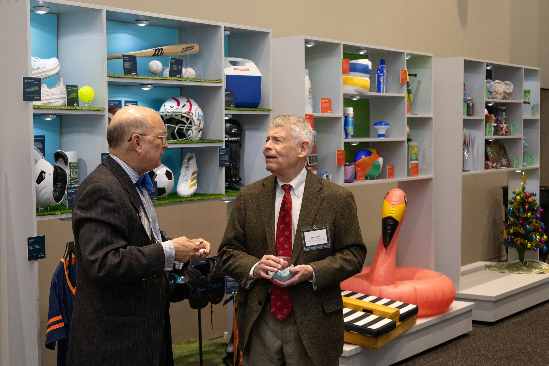 Two men in suits chatting in a colorful office display room with shelves of toys and objects.