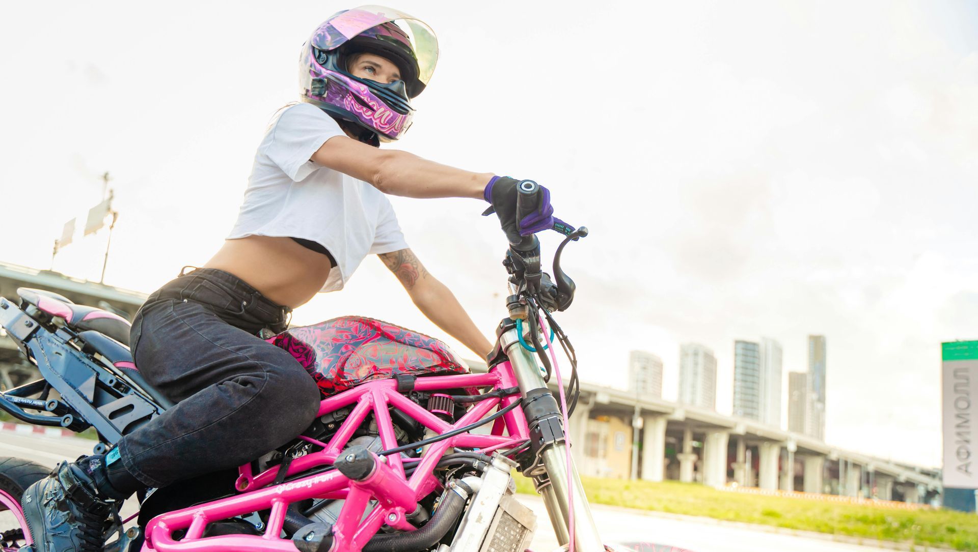 A woman is sitting on a pink motorcycle wearing a helmet.