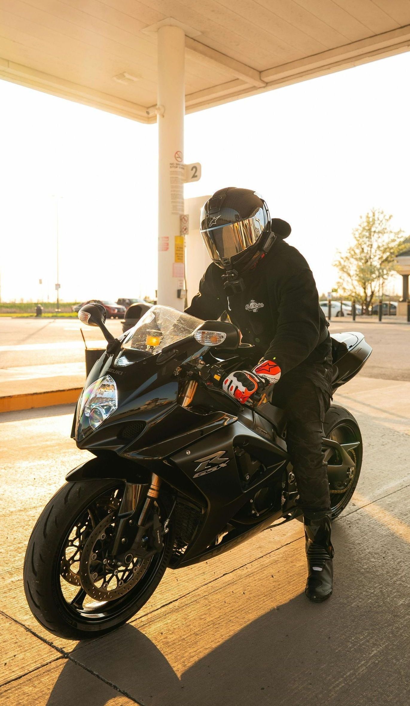 A man is standing on a motorcycle in a parking lot.
