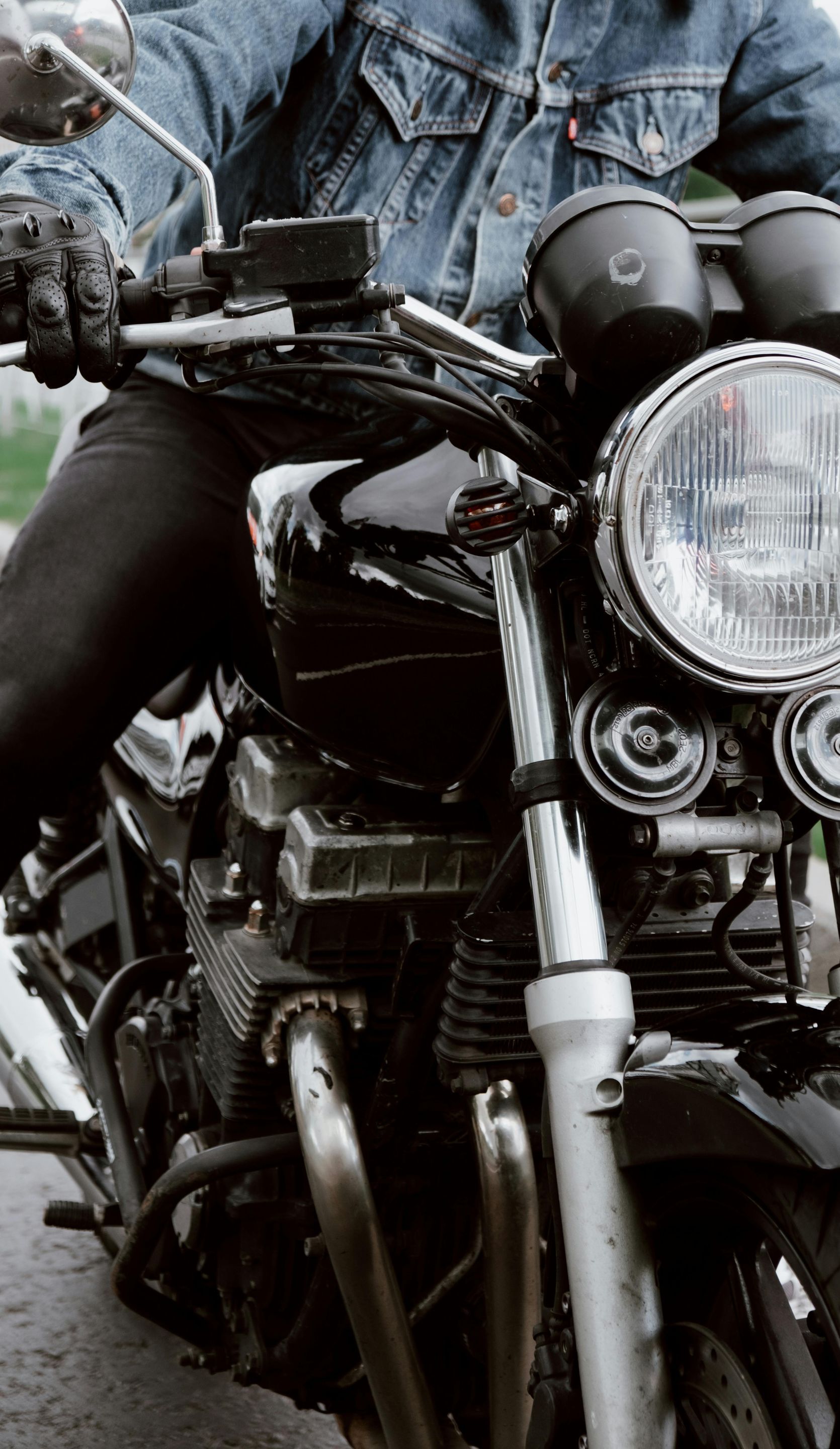 A man in a denim jacket is riding a black motorcycle.