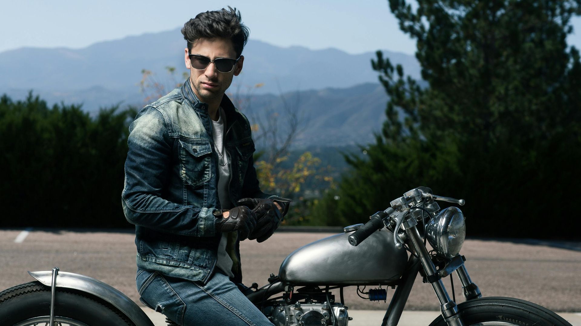 A man in a denim jacket is sitting on a motorcycle.