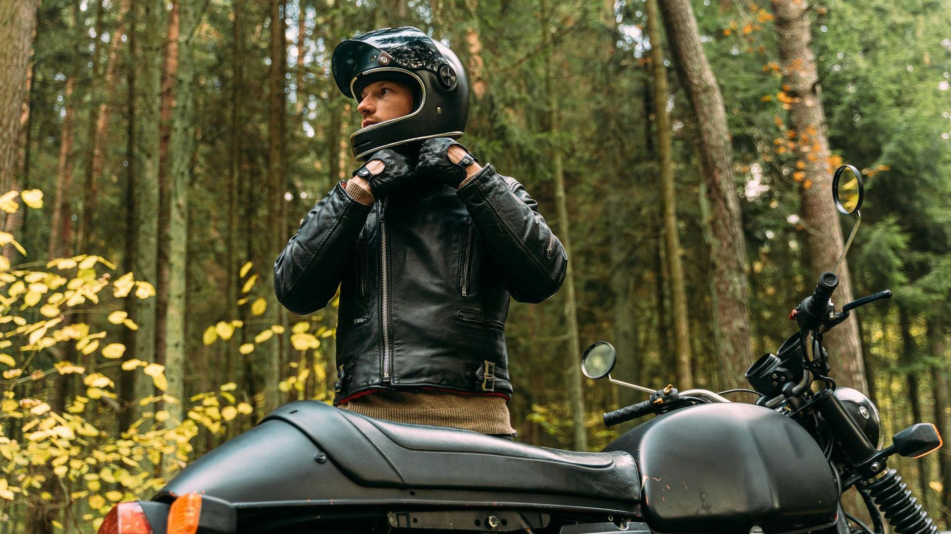 A man wearing a helmet is standing next to a motorcycle in the woods.