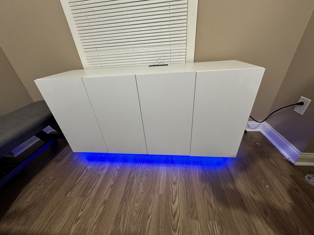 A white cabinet with blue lights underneath it is sitting on a wooden floor.