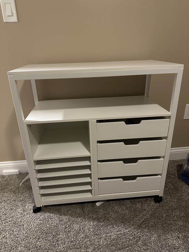 A white cabinet with drawers and shelves is sitting on a carpet in a room.