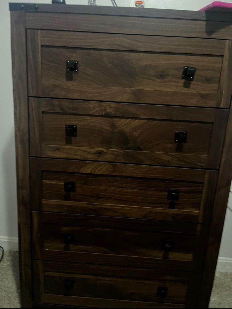 A wooden chest of drawers is sitting on the floor in a bedroom.
