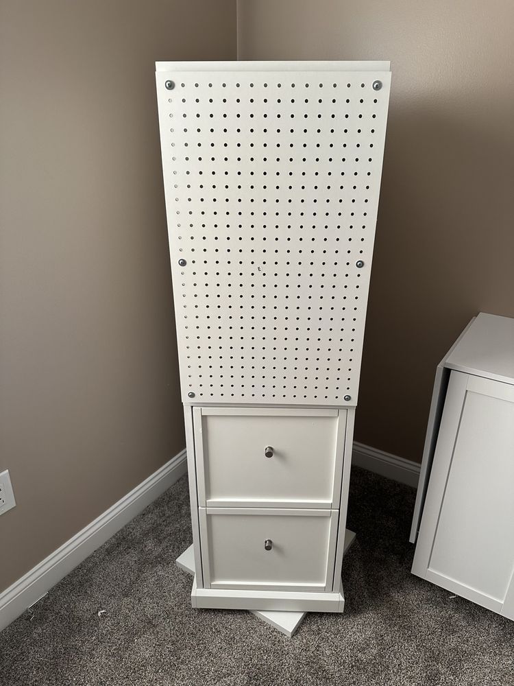 A white cabinet with two drawers and a pegboard on top of it.