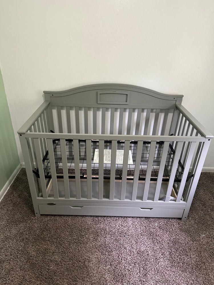 A gray crib is sitting on top of a carpeted floor in a room.