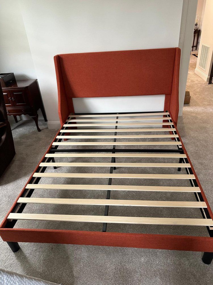 A bed frame with an orange headboard is sitting in a room.