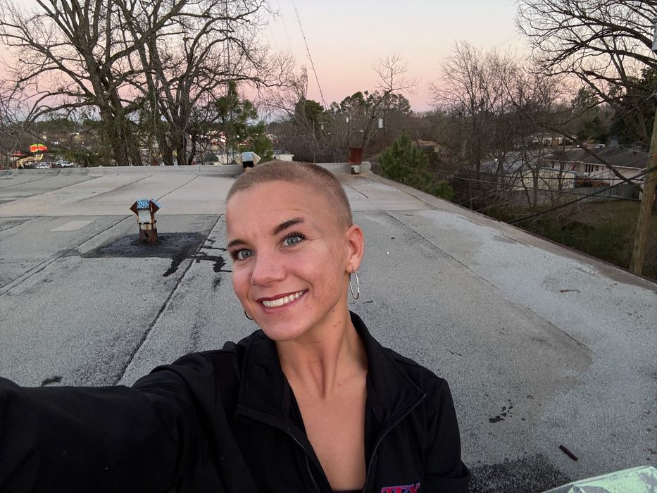 A woman with a shaved head is taking a selfie on a rooftop.