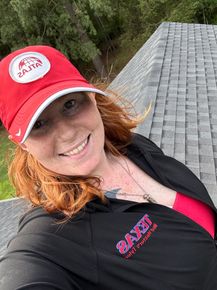A woman wearing a red hat and a black shirt is standing on a roof.