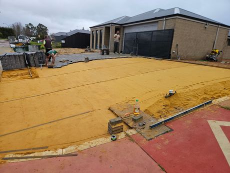 A group of people are working on a driveway in front of a house.