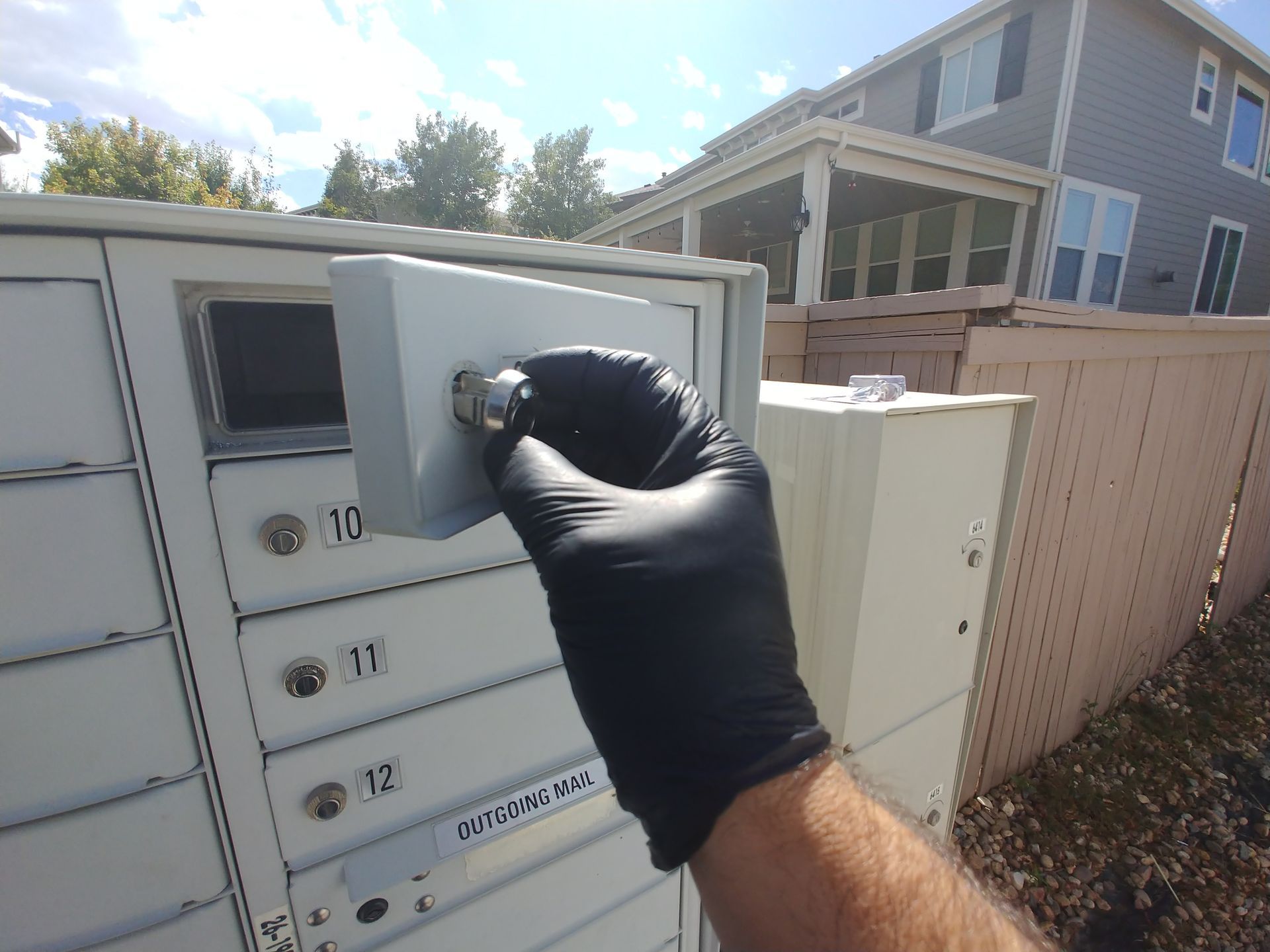 A person wearing black gloves is opening a mailbox