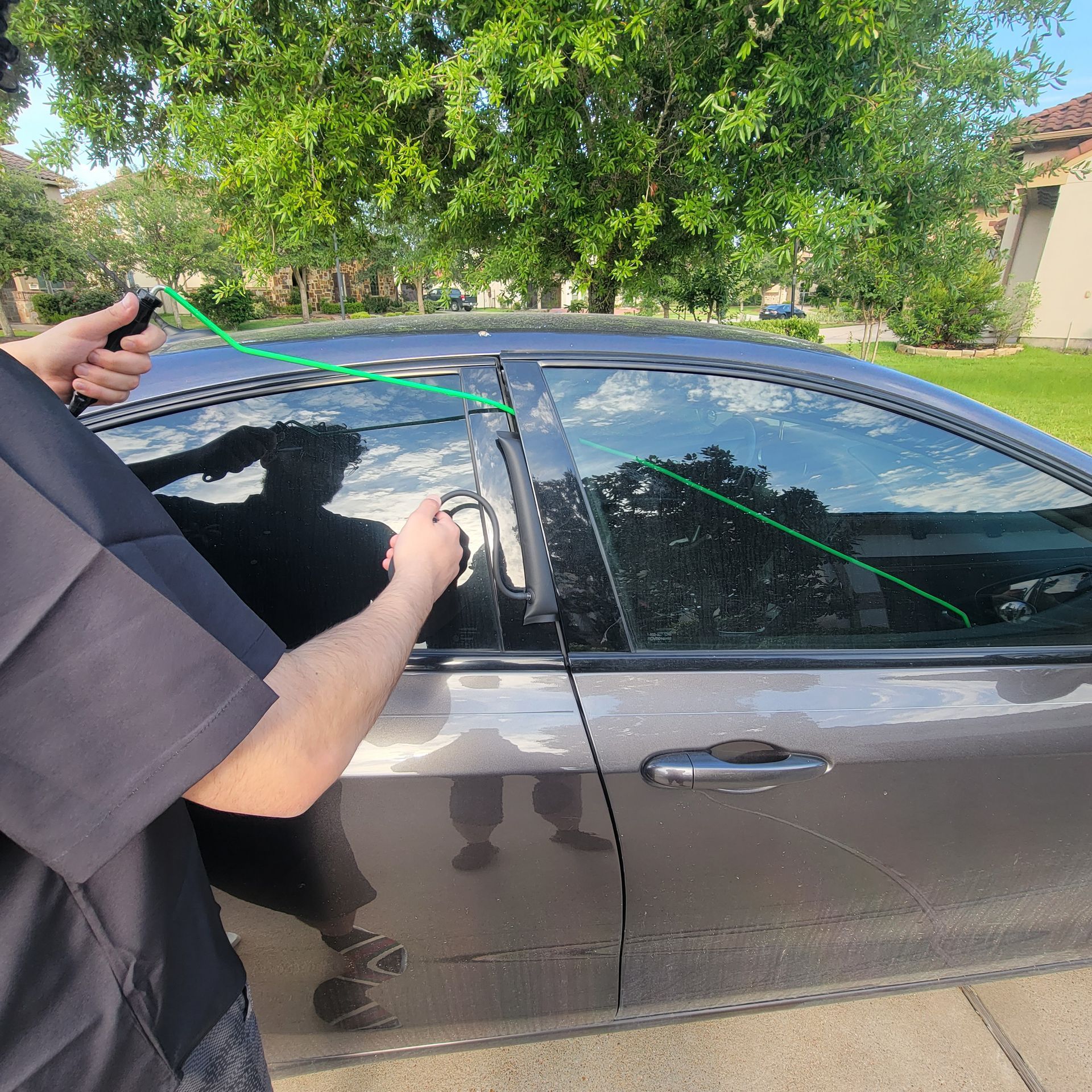 A man is using a green lockout tool to open a car door