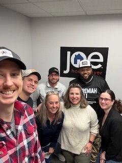 Group of people smiling in an office; logo on wall that says 