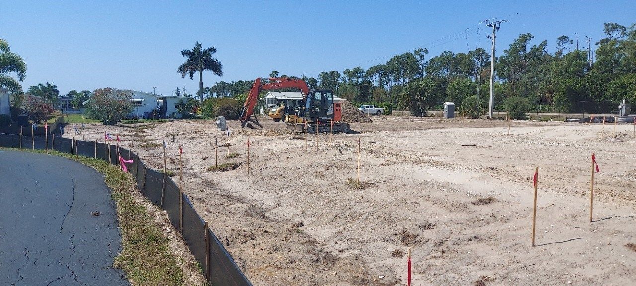 A large excavator is working on a dirt field next to a road.