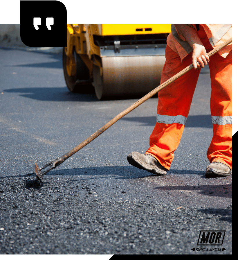 A man in orange pants is using a broom to spread asphalt on a road.