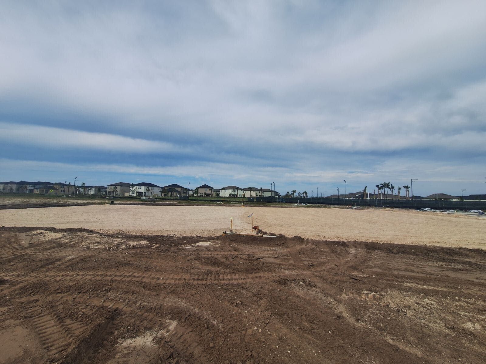 A large dirt field with houses in the background.
