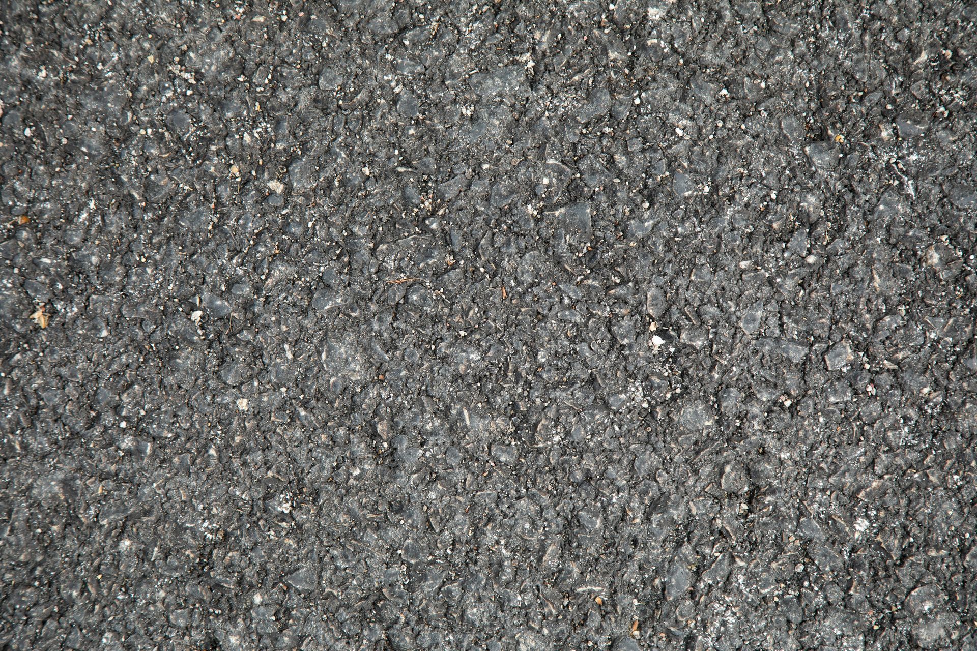 Close-up view of black asphalt road surface with small stones and grainy texture.