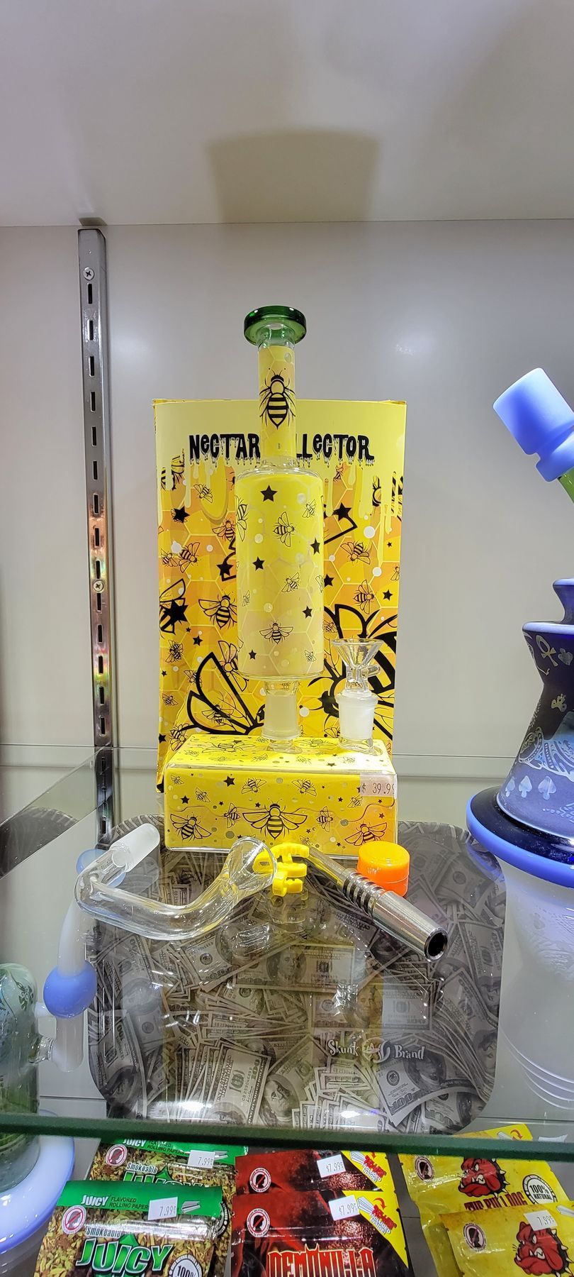 A yellow glass water pipe with bee designs sits on a shelf.