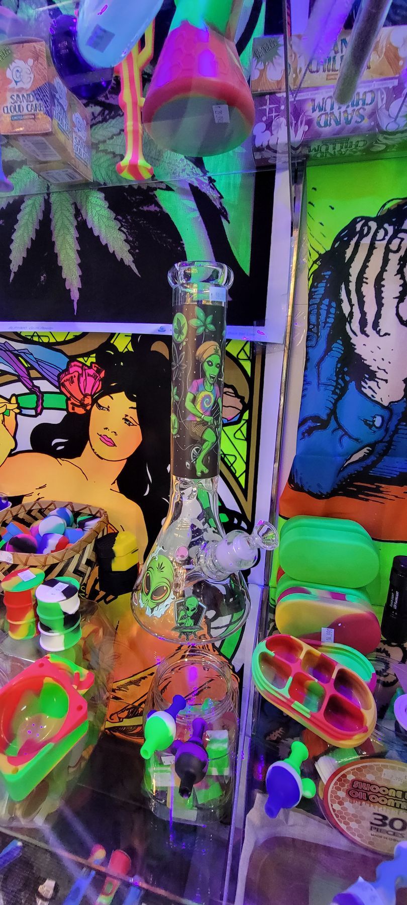 A glass bong surrounded by neon-colored items, with marijuana leaf posters in the background.