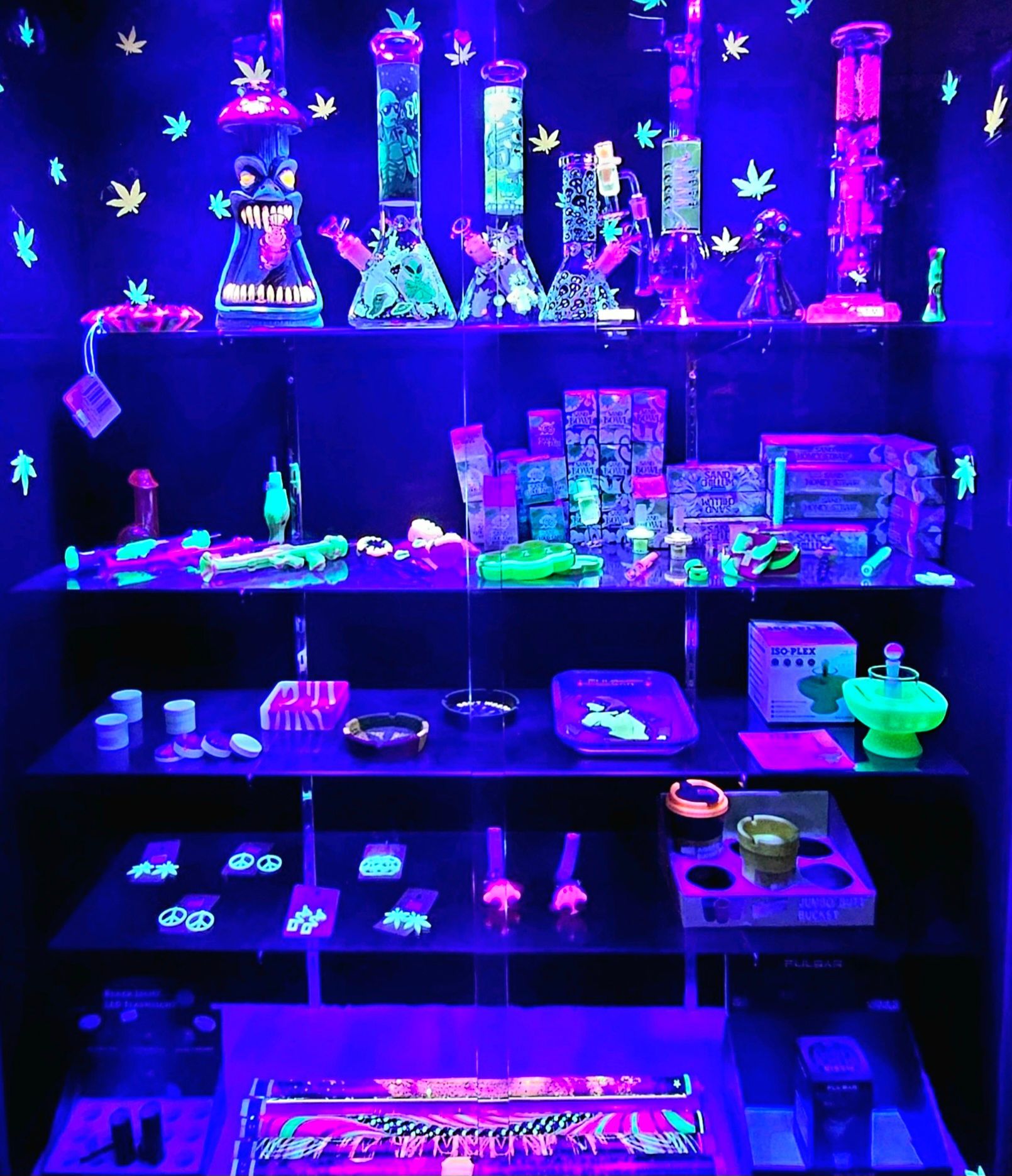 Blacklit display of colorful glass bongs and smoking accessories in a shop.