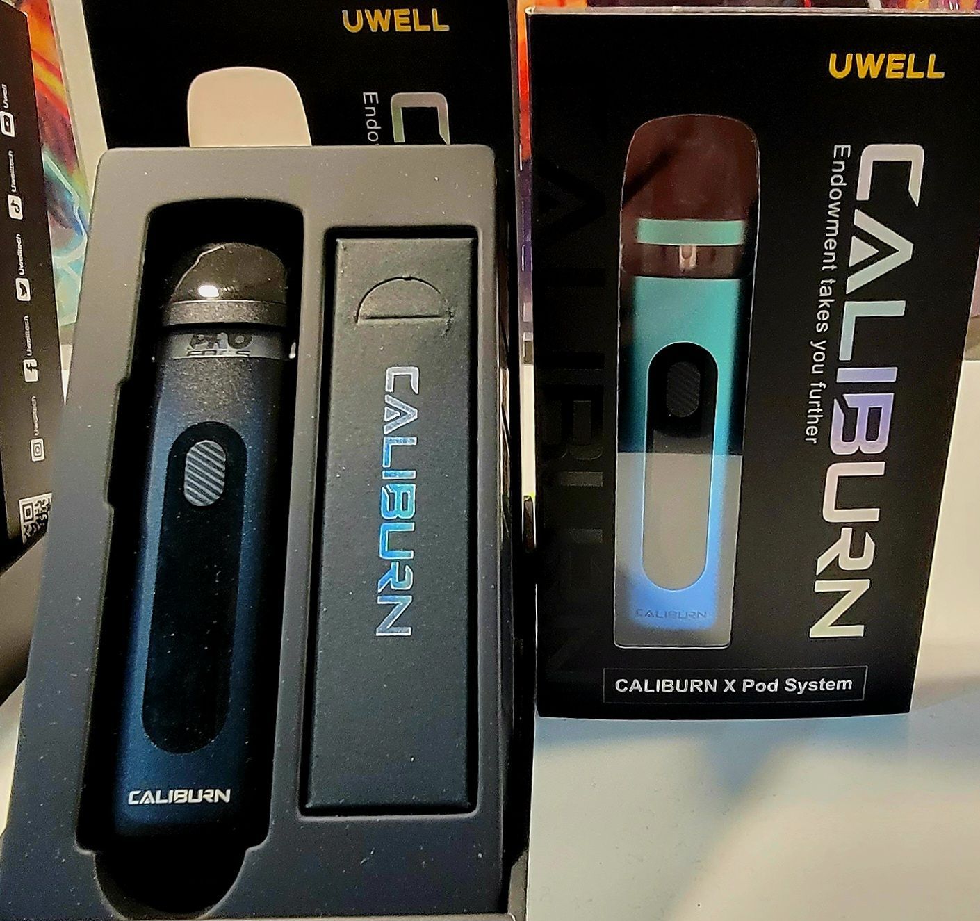 Two Uwell Caliburn X pod system boxes, one open showing a black device, the other a teal device.