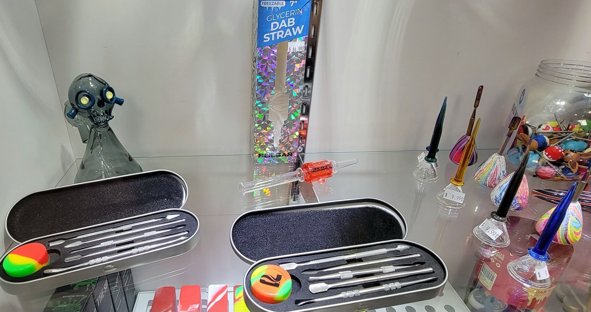 Display case with dab tools, a glass skull, and colorful accessories.