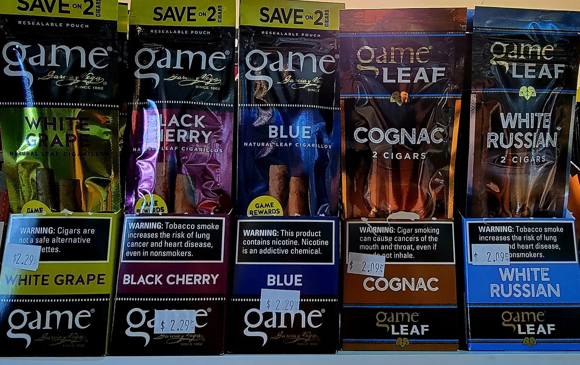 Display of Game Leaf tobacco wraps in various flavors like White Grape, Black Cherry, Blue, Cognac, and White Russian.