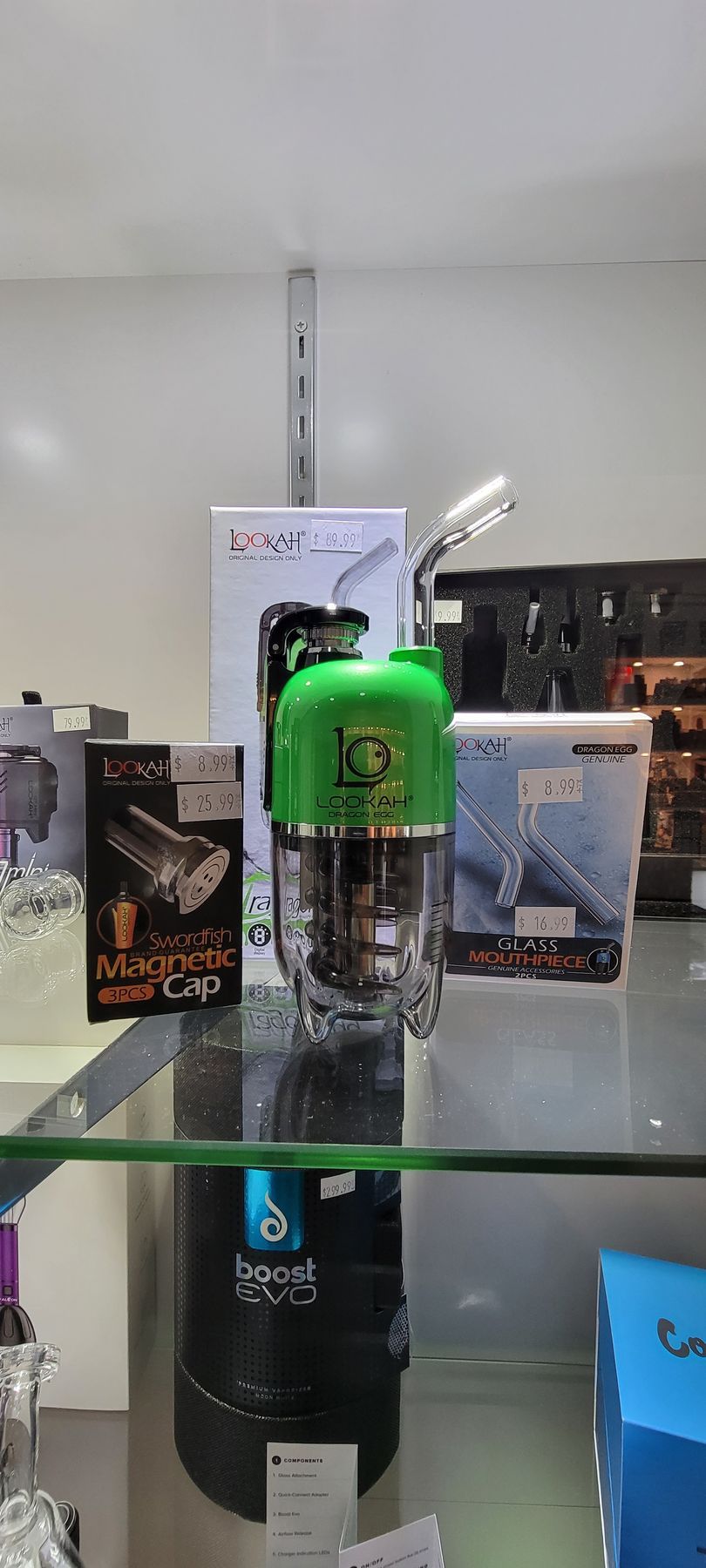 A glass and green vaporizer on a shelf in a shop, with various product boxes in the background.