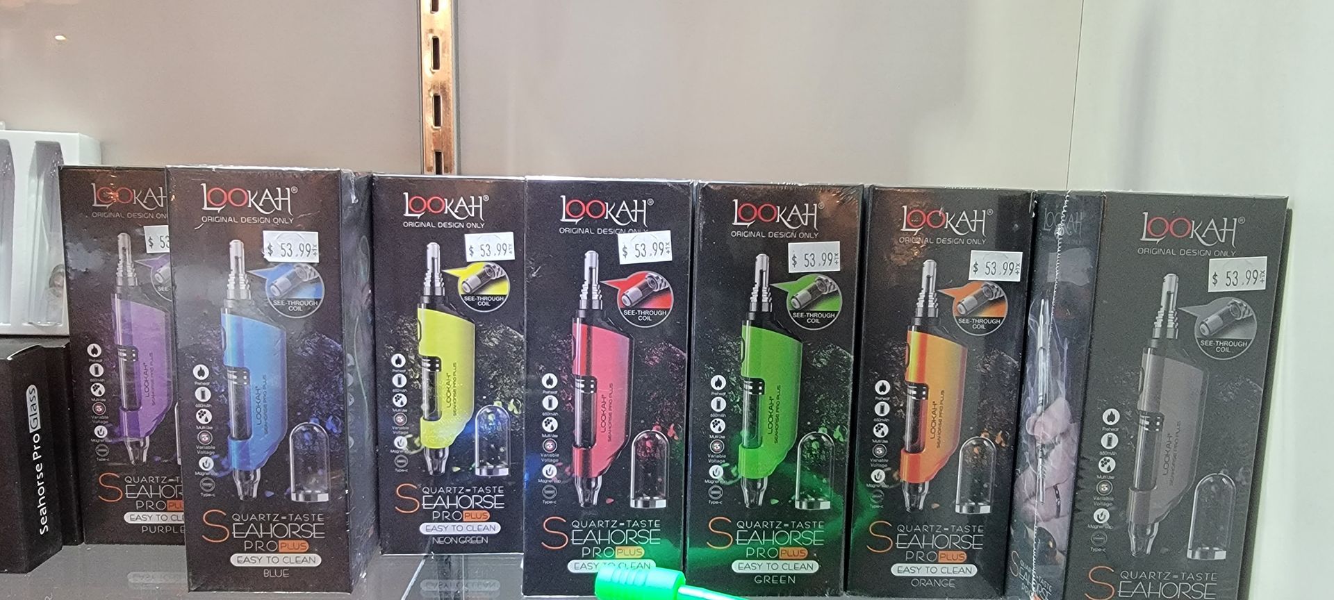 Various colored vape pen boxes displayed on a shelf, lit by overhead lighting.