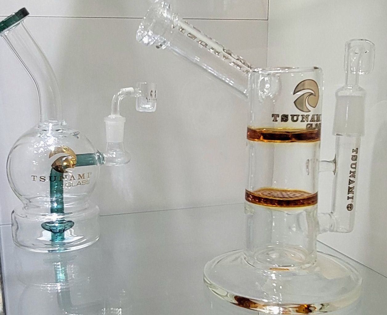 Two glass bongs displayed on a shelf. One is globe-shaped with teal accents. The other is a straight tube style.