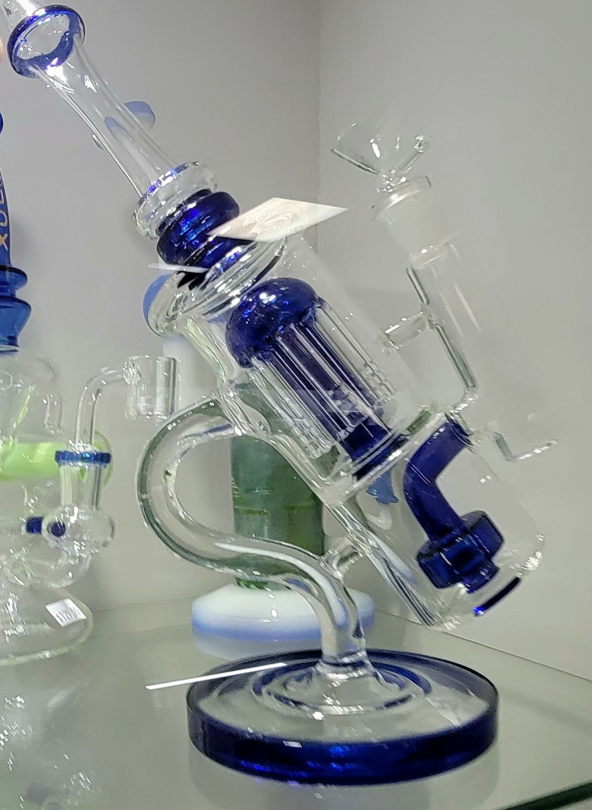 Blue and clear glass water pipe with a bubbler and circular base, displayed on a shelf.