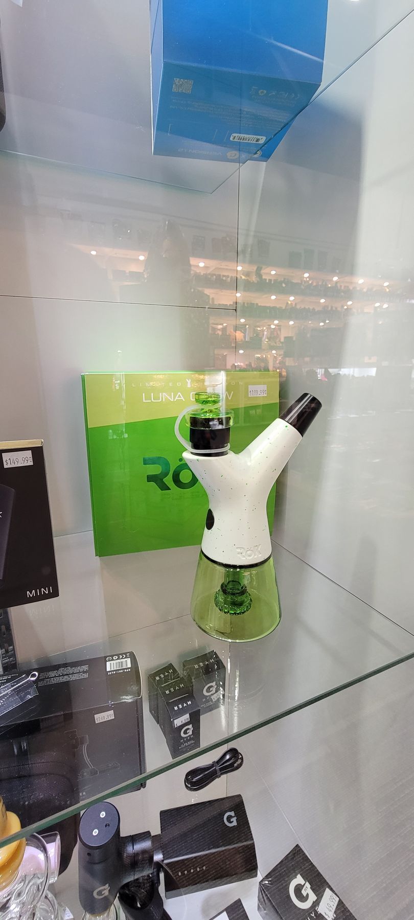 A glass display case with a white and green bong, other vaping supplies, and a green box with 