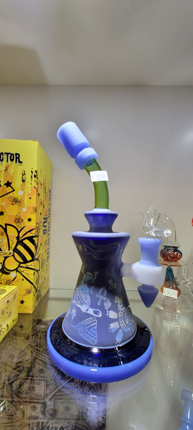 A blue and purple glass water pipe with a bent neck, displayed in a shop with a yellow box.
