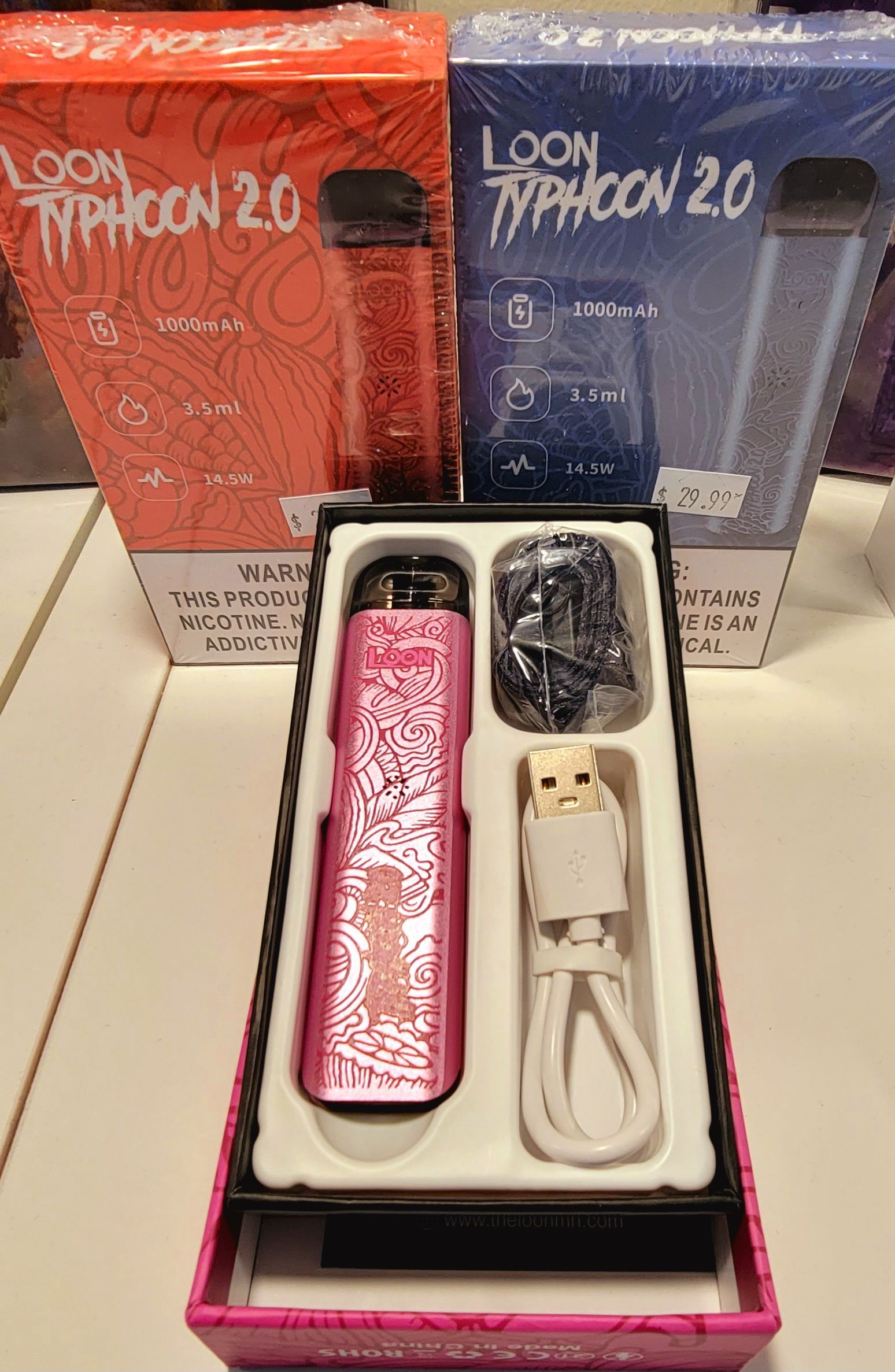 Pink Loon Typhoon 2.0 vape pen in open box, with charger and pods. Two boxes in background.