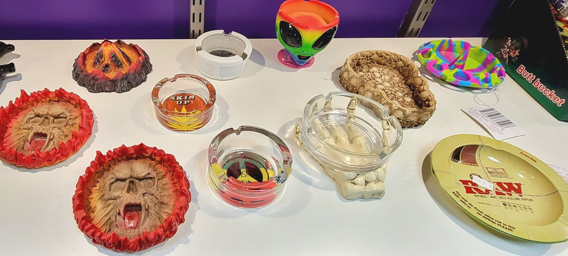 Various ashtrays displayed on a white surface, including lion faces, an alien, and colorful patterns.