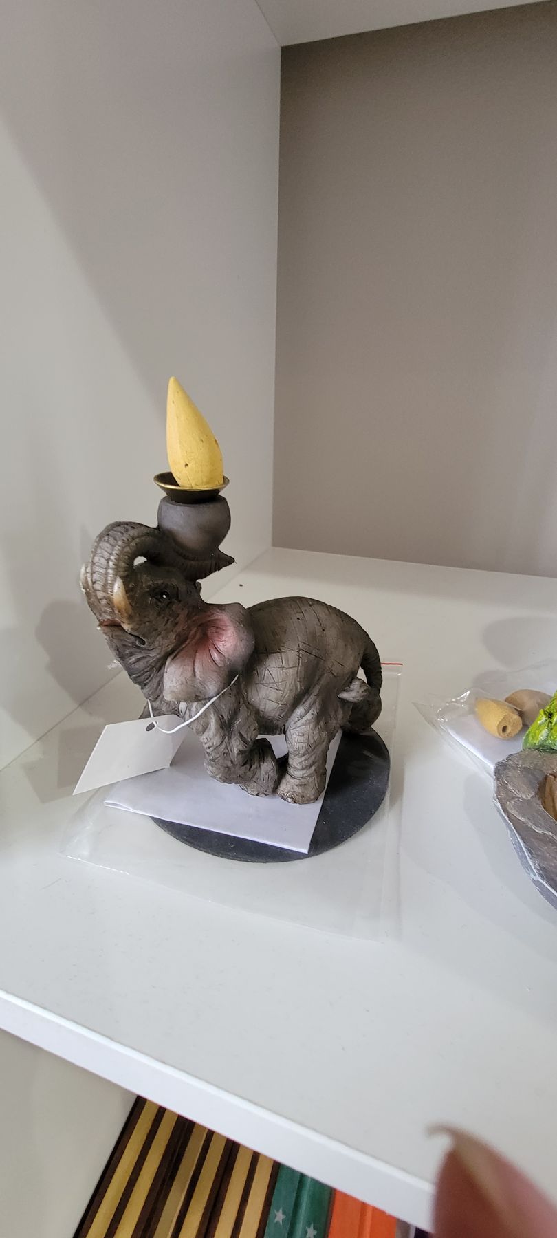 A gray elephant statue with a yellow cone on its head, standing on a white shelf.