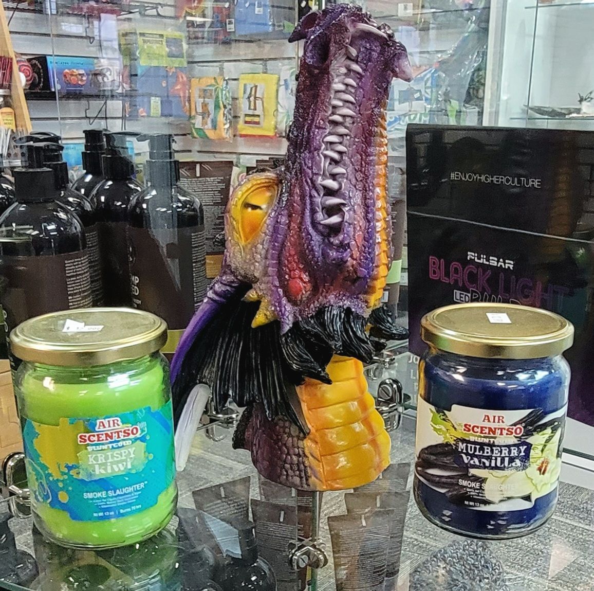 A store display featuring a dragon figurine between two jar candles, and bottles of beauty products.