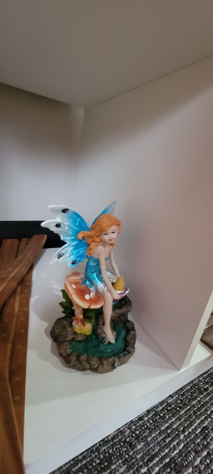 A fairy figurine with blue wings sits on a mushroom, holding a golden object.