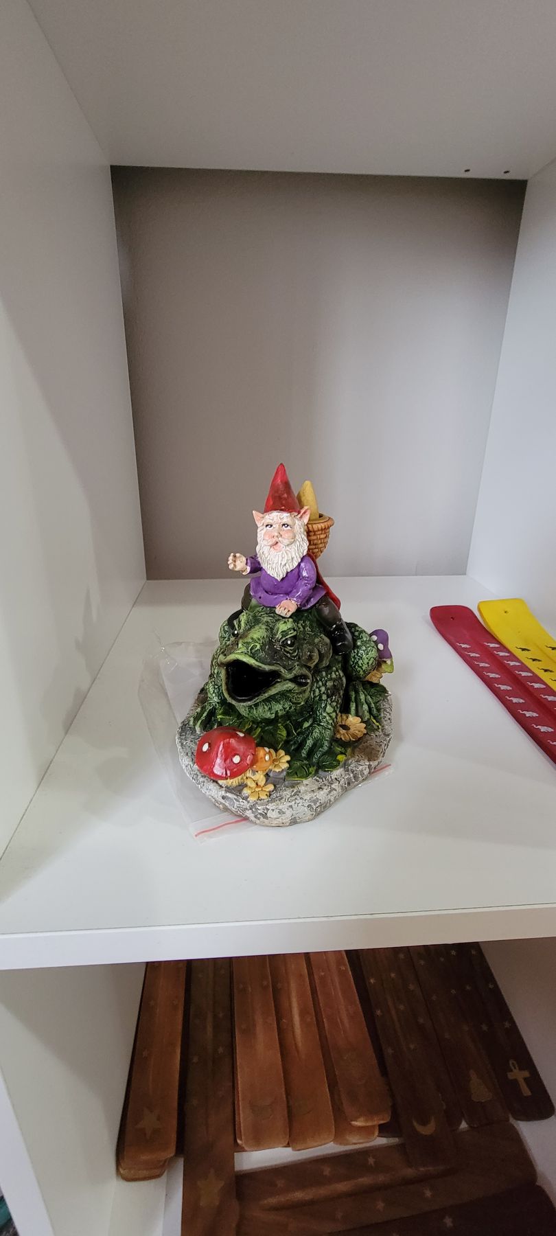 Gnome figurine on a rocky structure with red mushroom in a white-walled cabinet.
