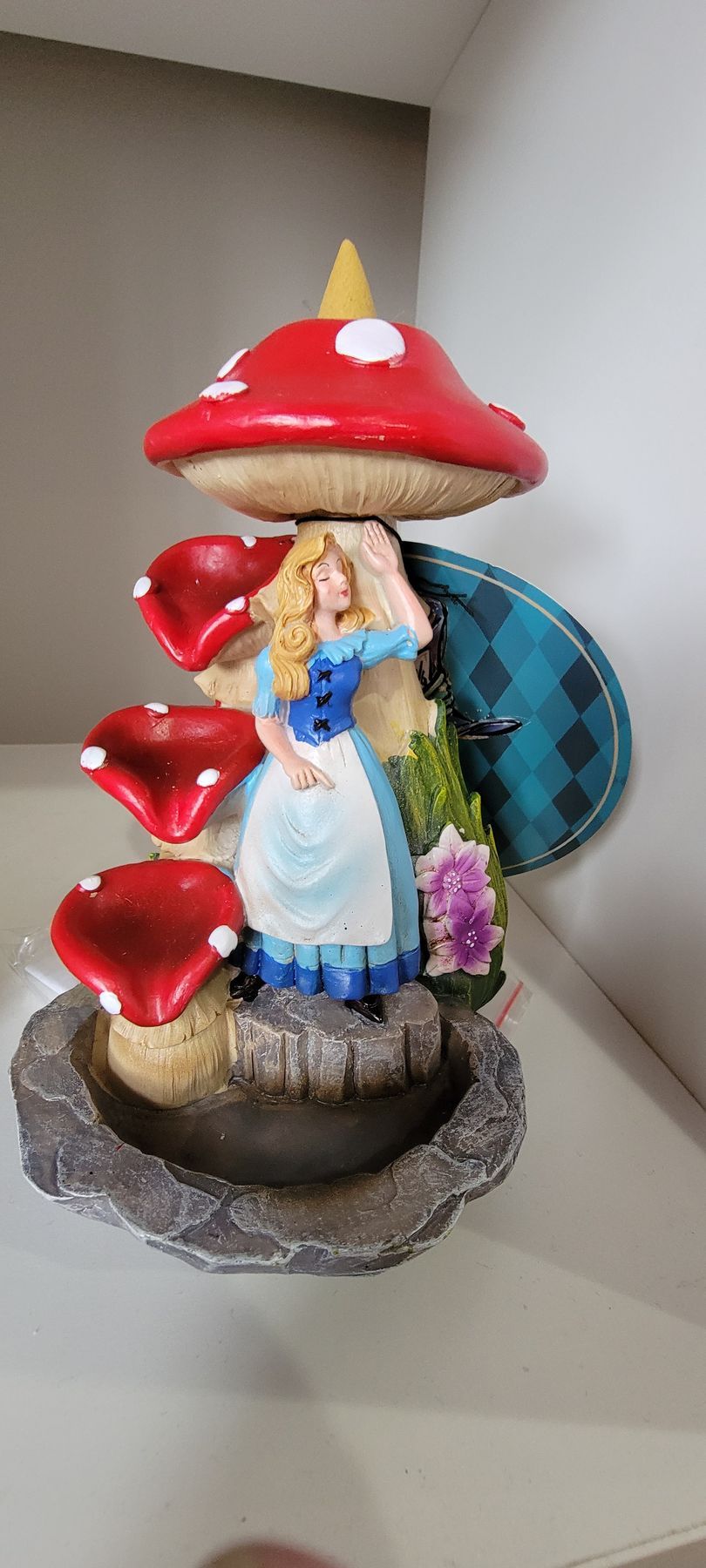 Alice in Wonderland figurine with mushrooms. Alice stands on a stone base, holding up a red mushroom.