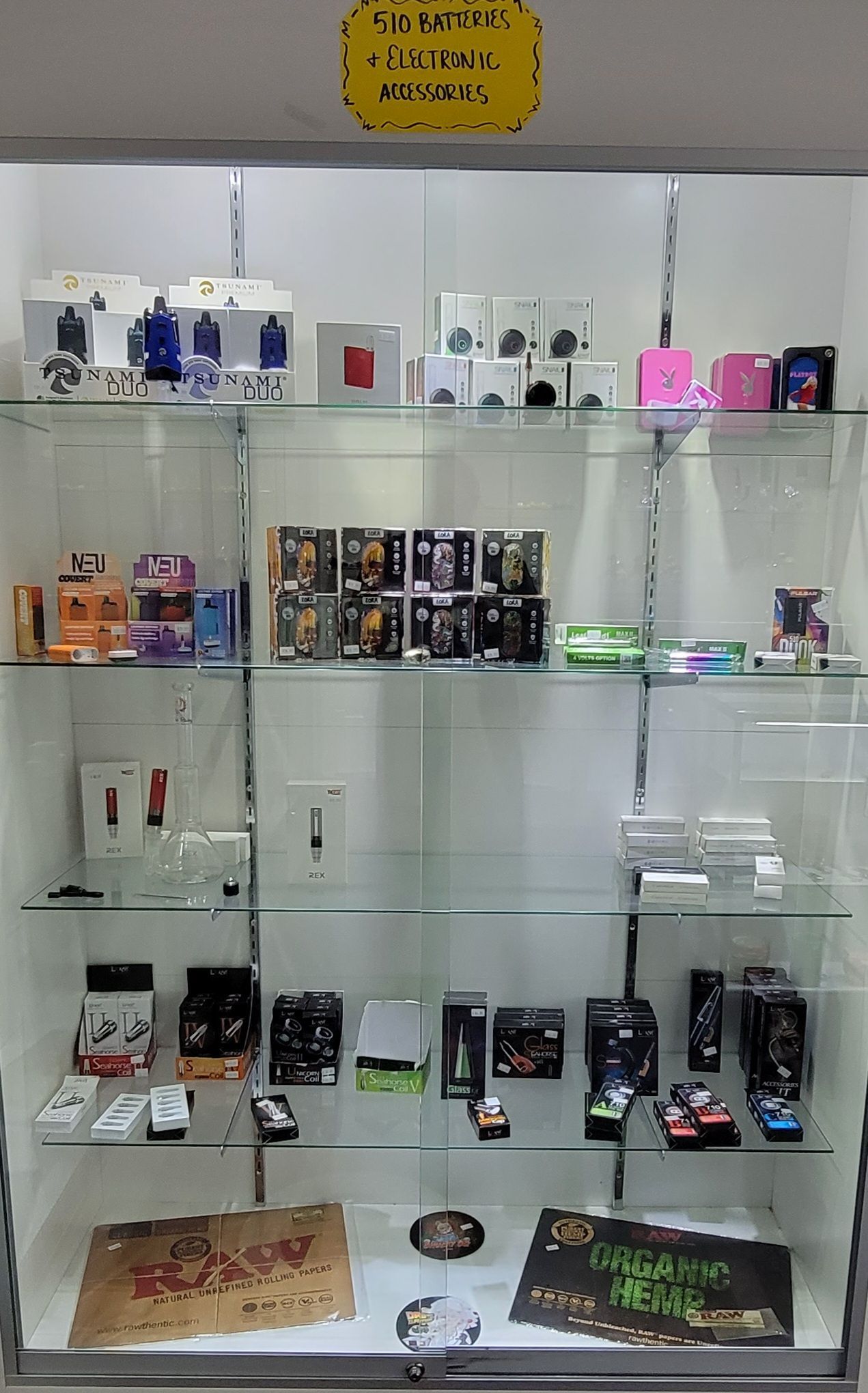Glass display case filled with various vaping devices, accessories, and products, illuminated inside a store.